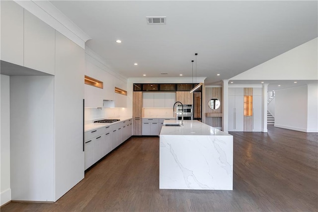 kitchen featuring a kitchen island with sink, stainless steel gas cooktop, sink, white cabinetry, and hanging light fixtures