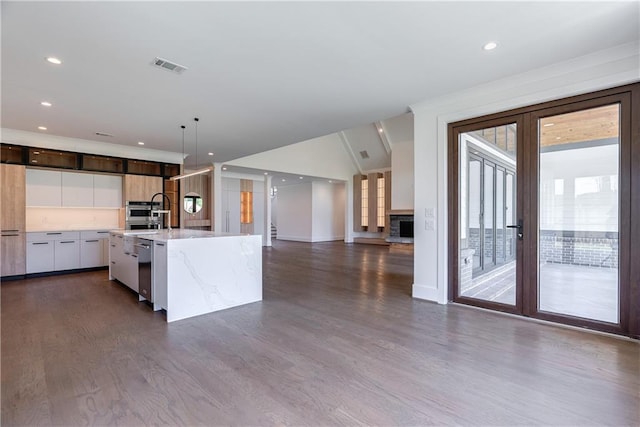 kitchen featuring pendant lighting, dark hardwood / wood-style floors, light stone countertops, an island with sink, and white cabinetry