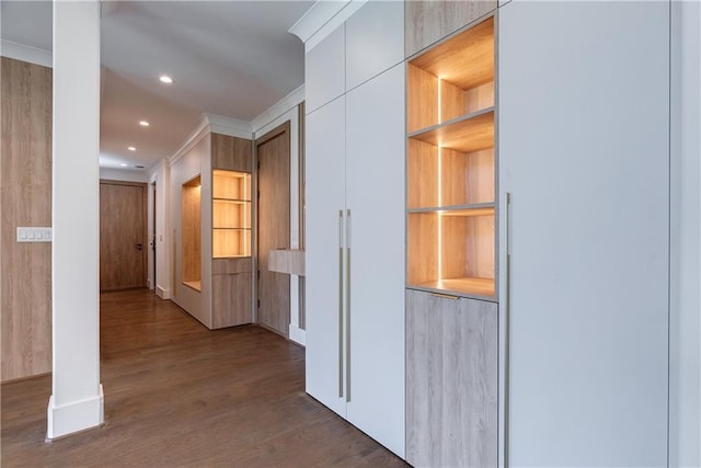 hallway with built in features, dark wood-type flooring, and ornamental molding