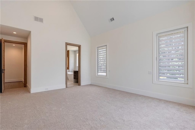 unfurnished bedroom featuring high vaulted ceiling, ensuite bath, multiple windows, and light colored carpet