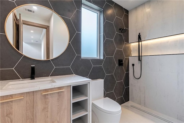 bathroom with vanity, toilet, tile walls, tasteful backsplash, and a tile shower