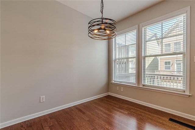 empty room with dark hardwood / wood-style flooring and an inviting chandelier