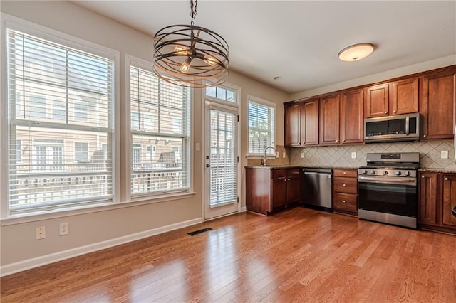 kitchen with decorative backsplash, appliances with stainless steel finishes, sink, pendant lighting, and stone countertops