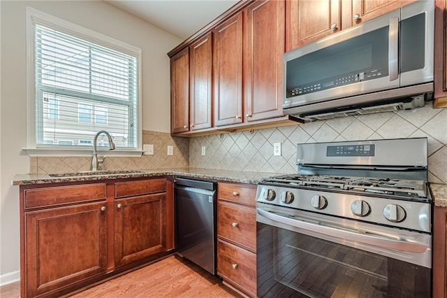 kitchen with stone counters, sink, light wood-type flooring, and appliances with stainless steel finishes