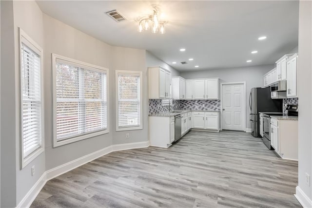 kitchen featuring backsplash, white cabinets, light wood-type flooring, appliances with stainless steel finishes, and light stone counters