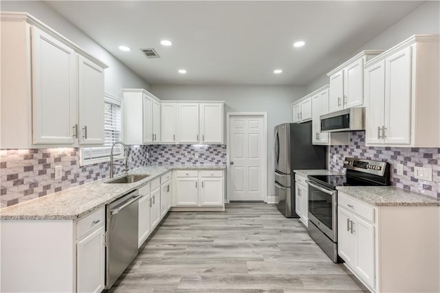 kitchen featuring white cabinets, sink, light stone countertops, appliances with stainless steel finishes, and light hardwood / wood-style floors