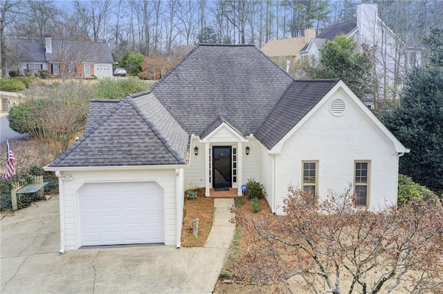 view of front of property with driveway, a garage, brick siding, and roof with shingles