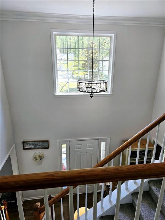 staircase with crown molding, a healthy amount of sunlight, wood-type flooring, and a notable chandelier