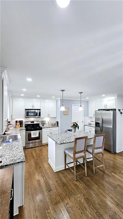 kitchen with pendant lighting, sink, appliances with stainless steel finishes, white cabinetry, and a kitchen island