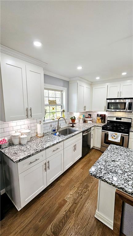 kitchen featuring appliances with stainless steel finishes, sink, white cabinets, dark hardwood / wood-style flooring, and light stone countertops