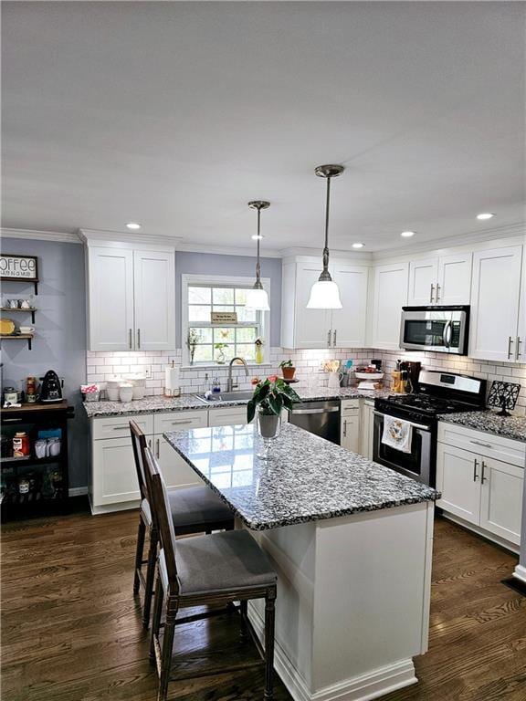 kitchen with sink, hanging light fixtures, stainless steel appliances, a center island, and white cabinets