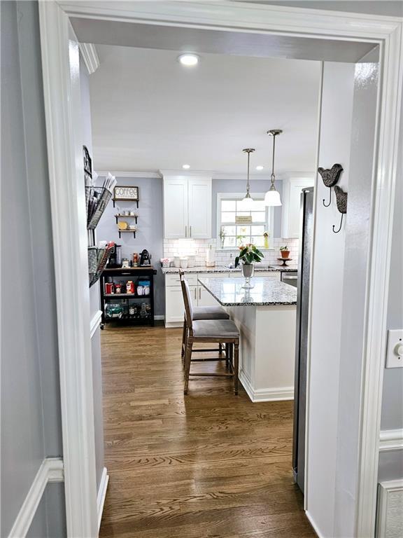 kitchen with a breakfast bar area, hanging light fixtures, dark hardwood / wood-style floors, light stone countertops, and white cabinets