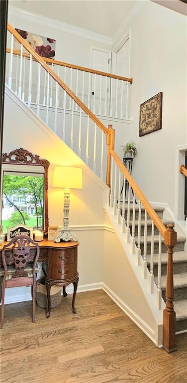 stairway with a towering ceiling, wood-type flooring, and ornamental molding