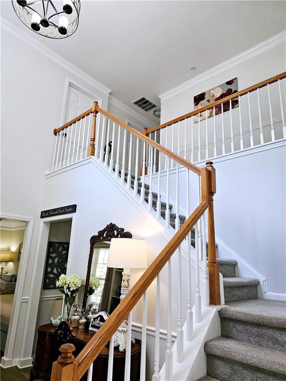 stairway featuring crown molding, an inviting chandelier, and a high ceiling