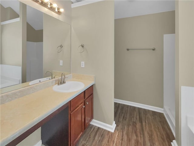 bathroom with vanity, a bath, wood finished floors, and baseboards