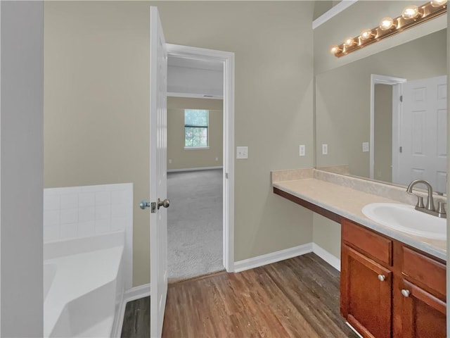 full bathroom with vanity, a bath, wood finished floors, and baseboards