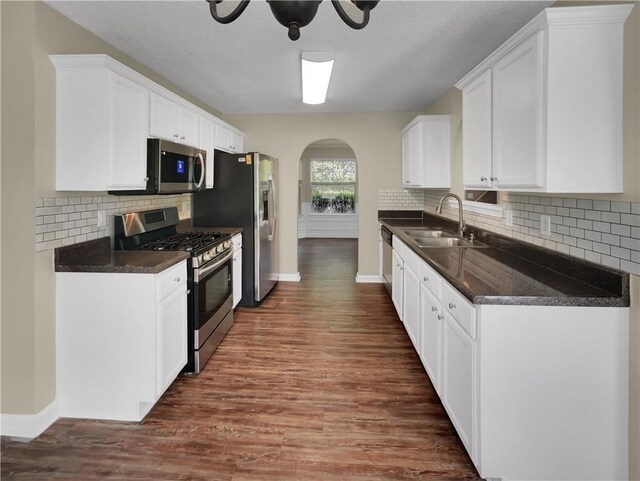 kitchen with appliances with stainless steel finishes, white cabinetry, sink, dark wood-type flooring, and tasteful backsplash