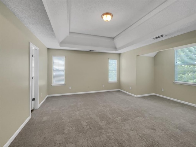 unfurnished room featuring a raised ceiling, a healthy amount of sunlight, visible vents, and a textured ceiling