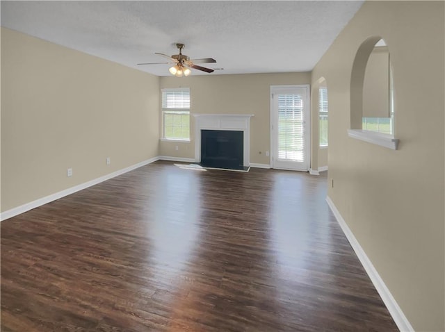 unfurnished living room with ceiling fan, baseboards, dark wood finished floors, a fireplace, and a textured ceiling