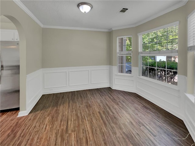 unfurnished room with a wainscoted wall, visible vents, arched walkways, dark wood-style flooring, and ornamental molding