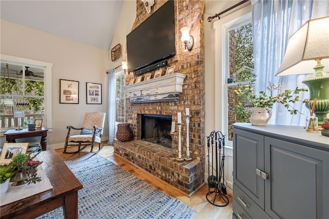 living area with lofted ceiling, a healthy amount of sunlight, light wood-style flooring, and a fireplace
