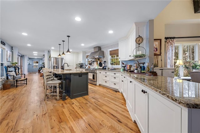kitchen featuring appliances with stainless steel finishes, white cabinets, a kitchen bar, and wall chimney exhaust hood