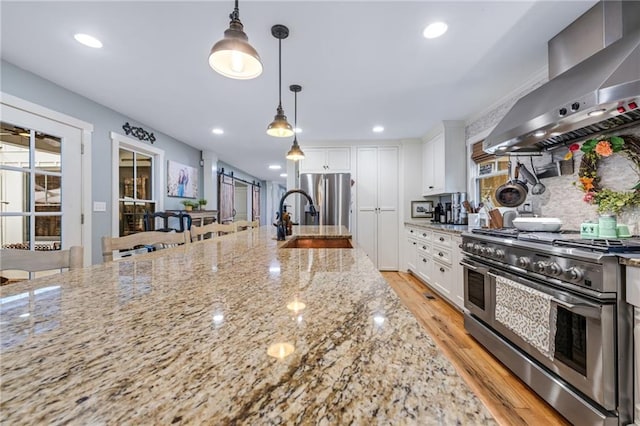 kitchen featuring appliances with stainless steel finishes, white cabinetry, a sink, light wood finished floors, and wall chimney exhaust hood