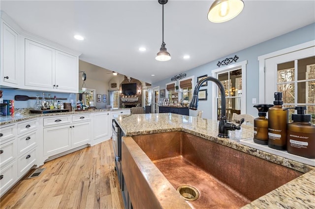 kitchen with decorative light fixtures, visible vents, a sink, white cabinets, and light wood-style flooring