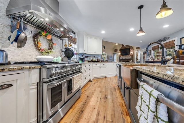 kitchen featuring appliances with stainless steel finishes, light stone countertops, white cabinets, light wood finished floors, and wall chimney exhaust hood