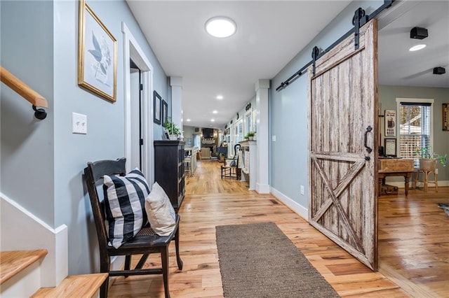 hall with baseboards, a barn door, and light wood-style floors