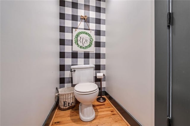 half bath featuring baseboards, wood finished floors, and toilet
