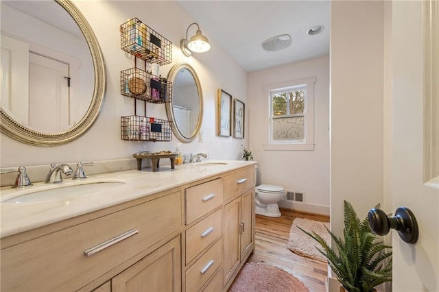 bathroom featuring a sink, toilet, wood finished floors, and visible vents