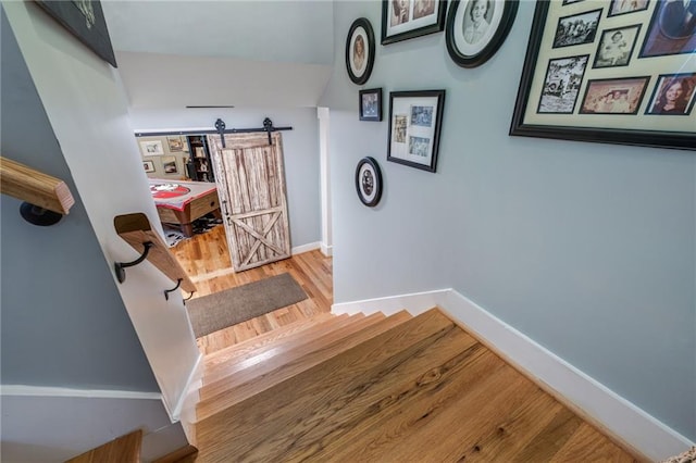 staircase with baseboards, a barn door, and wood finished floors