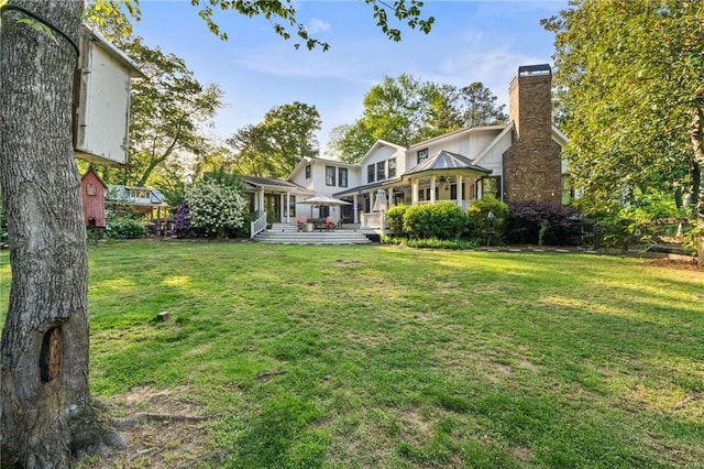 rear view of house with a lawn, a wooden deck, and a chimney
