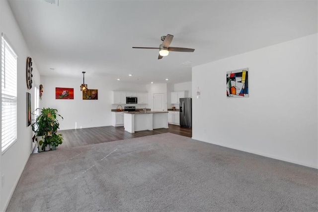 unfurnished living room with ceiling fan, a healthy amount of sunlight, and dark carpet