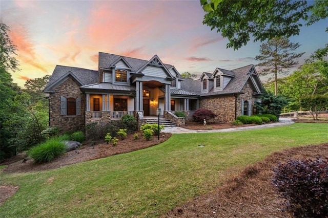 view of front of property with covered porch, stone siding, a front lawn, and a standing seam roof