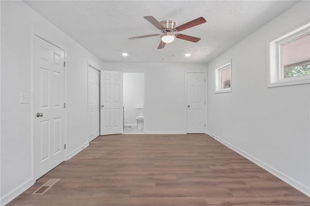 unfurnished bedroom featuring multiple closets, ceiling fan, ensuite bathroom, and dark hardwood / wood-style floors