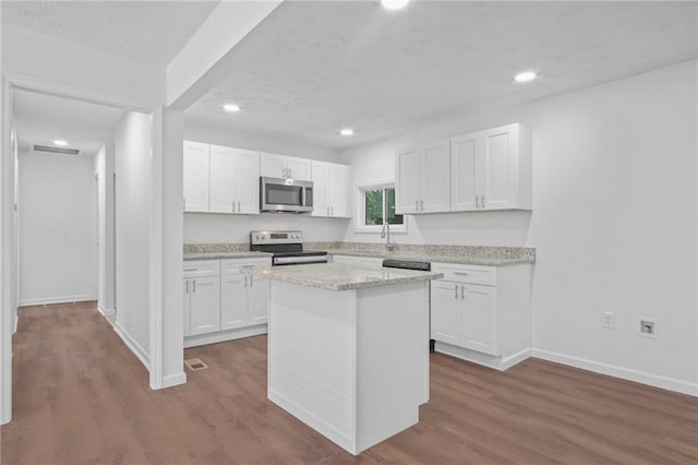 kitchen with light stone countertops, white cabinetry, a center island, wood-type flooring, and appliances with stainless steel finishes