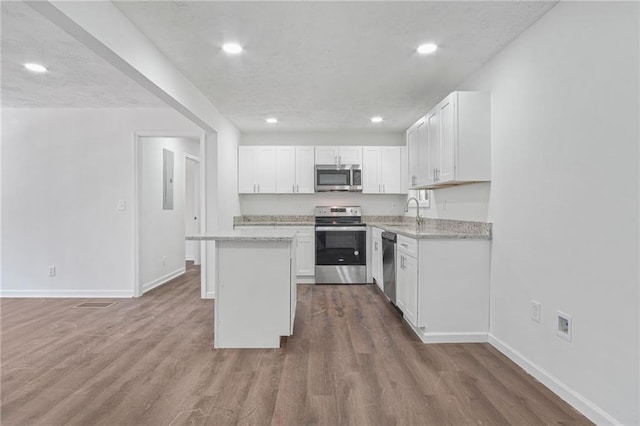 kitchen featuring white cabinets, appliances with stainless steel finishes, a center island, and light stone countertops