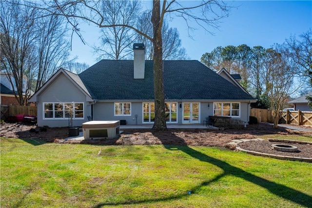 rear view of house featuring a hot tub, a yard, and a fire pit