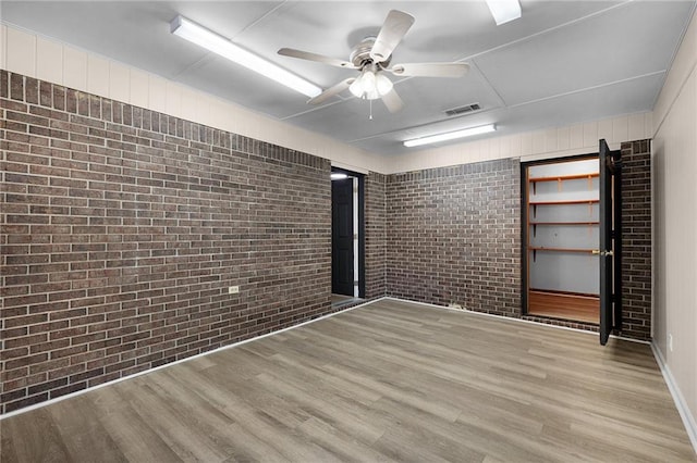 spare room with ceiling fan, light hardwood / wood-style floors, and brick wall