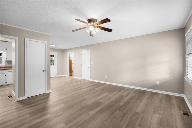 empty room with a textured ceiling, light hardwood / wood-style flooring, ceiling fan, and crown molding