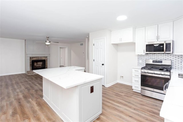 kitchen with stainless steel appliances, light stone countertops, ceiling fan, white cabinets, and backsplash