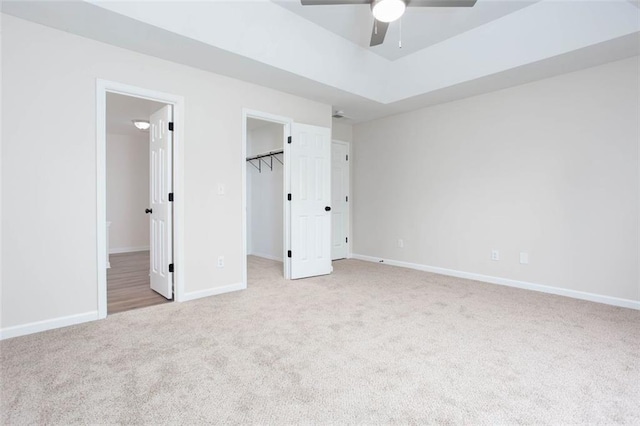 unfurnished bedroom featuring ensuite bathroom, ceiling fan, a closet, a walk in closet, and light colored carpet