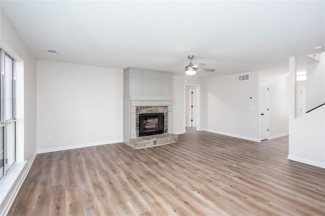 unfurnished living room featuring ceiling fan, light hardwood / wood-style floors, and a stone fireplace