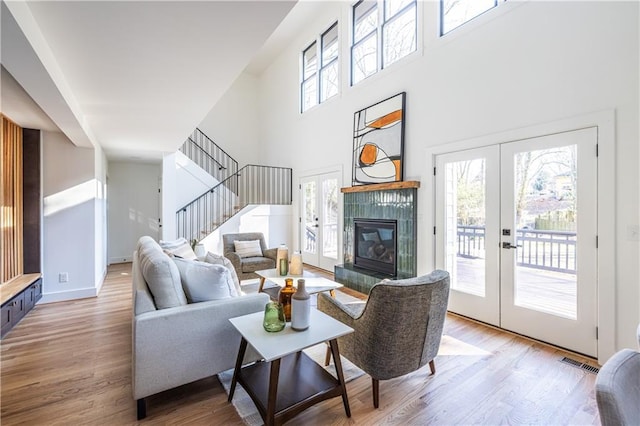 living room featuring hardwood / wood-style floors, a fireplace, a high ceiling, and french doors