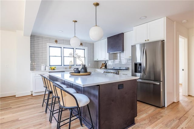 kitchen with white cabinetry, wall chimney range hood, stainless steel fridge with ice dispenser, a kitchen island, and range