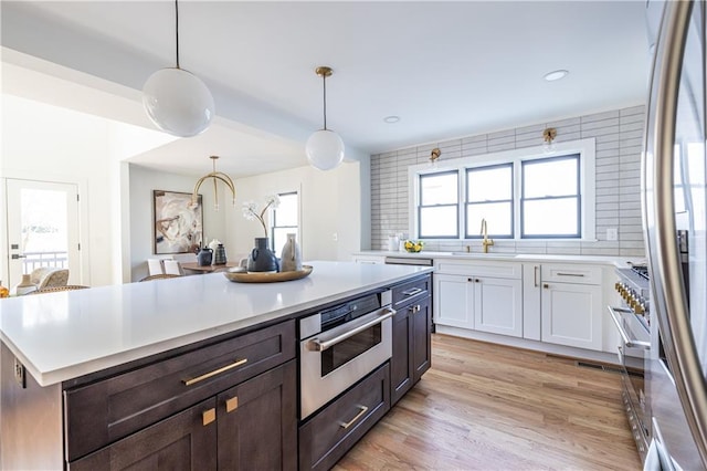 kitchen with appliances with stainless steel finishes, backsplash, decorative light fixtures, white cabinetry, and a kitchen island