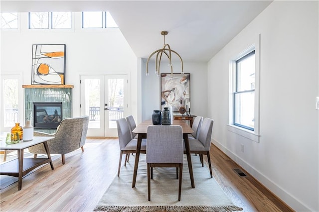 dining room featuring a tile fireplace, french doors, light hardwood / wood-style floors, and plenty of natural light