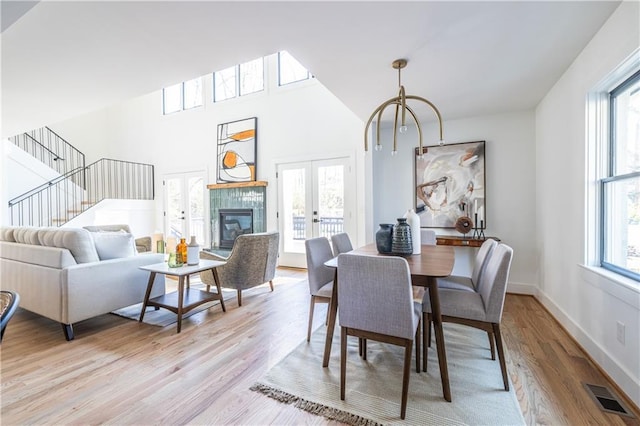 dining area featuring plenty of natural light, a tiled fireplace, light wood-type flooring, and french doors